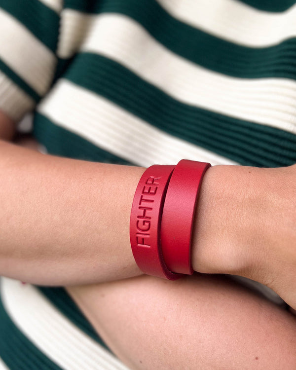 DUO læderarmbånd i rødt læder med graveringen "Fighter" viklet dobbelt om håndleddet, grøn-hvid stribet bluse