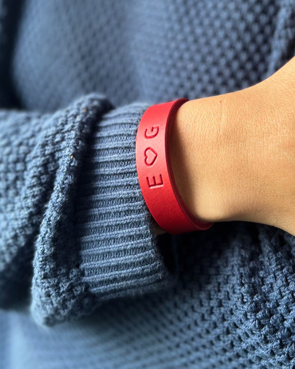 MONO læderarmbånd i rødt læder med initialerne "E ♡ G" graveret om håndleddet, båret til blå strik