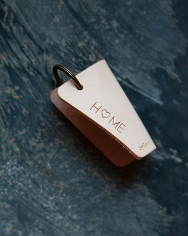 FOLD nøgleskjuler i naturfarvet læder med graveringen "Home" med hjerte som O, liggende på blå patineret overflade