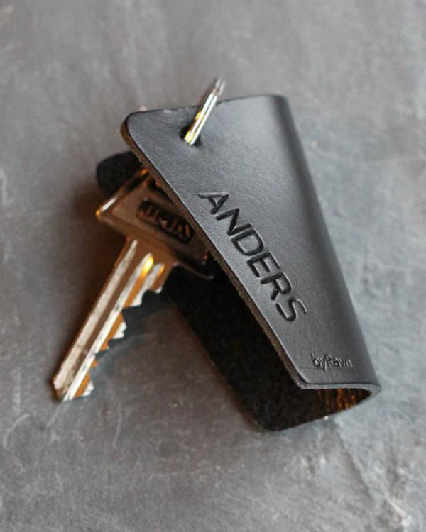 FOLD nøgleskjuler i sort læder med navnet "Anders" graveret, med nøgler på mørk skifer