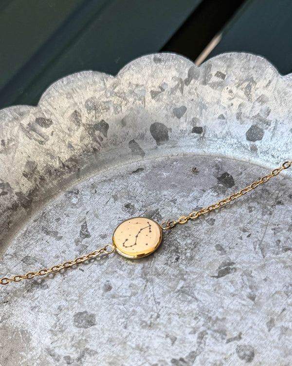 IBI STAR armbånd i guldbelagt stål med stjernebilledet Skorpionen graveret på rund plade, liggende på zinkfad