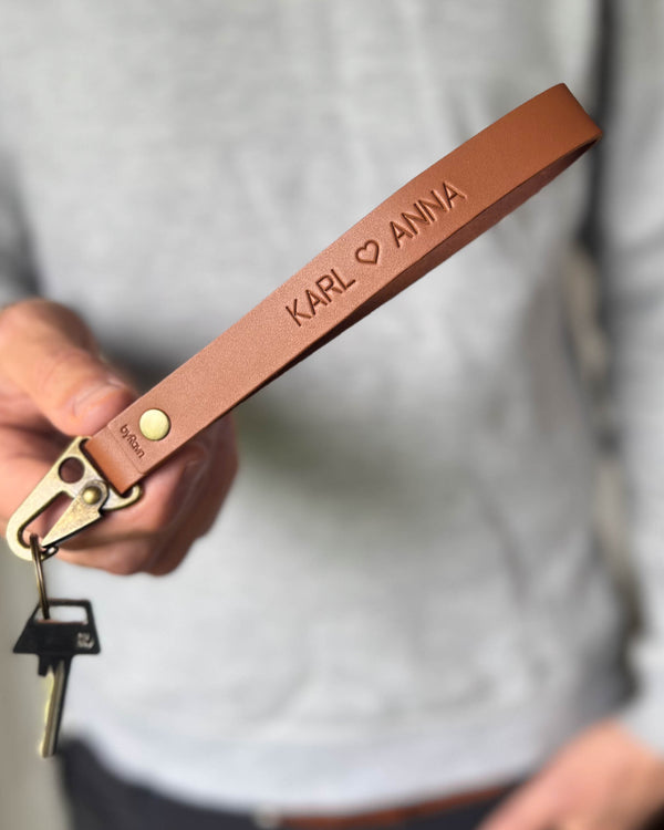 IRON nøglering i cognac læder med navnene "Karl ♡ Anna" graveret, holdt i hånden med nøgle