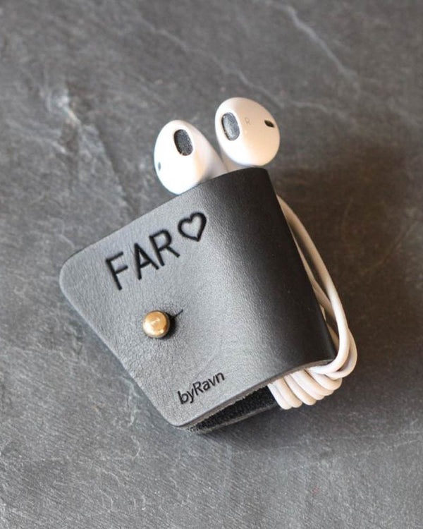 KAX høretelefonholder i sort læder med personlig gravering "Far" ♡ og messingknap, med earpods på mørk skifer