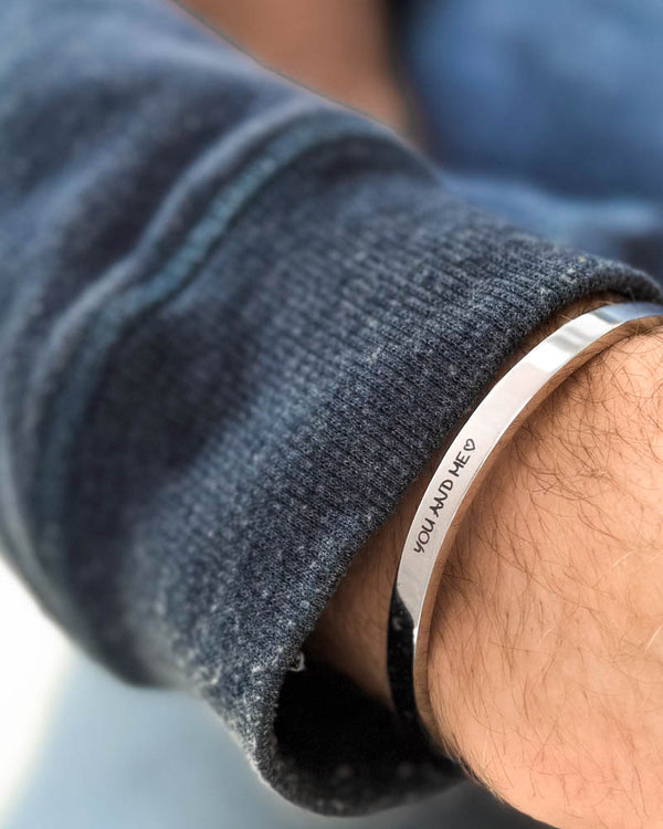 MARS SCRIPT armbånd i sølvfarvet rustfrit stål med "You and me" ♡ graveret i håndskrift om håndleddet, blå sweatshirt