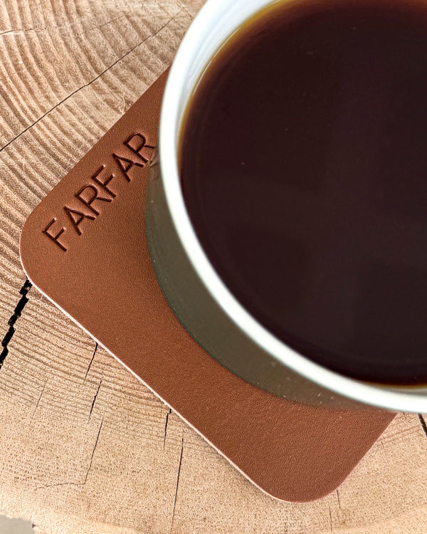 MOKKA firkantet bordskåner i cognac læder med graveringen "Farfar" under kop med kaffe på træskive