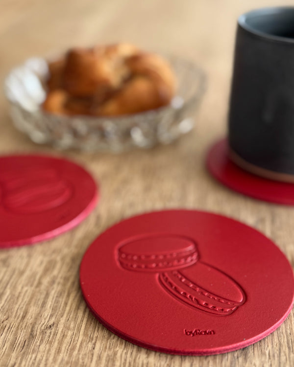 MOKKA kaffe & kage bordskåner i rødt læder præget med macarons på træbord ved sort kop og kanelsnegl i glasskål