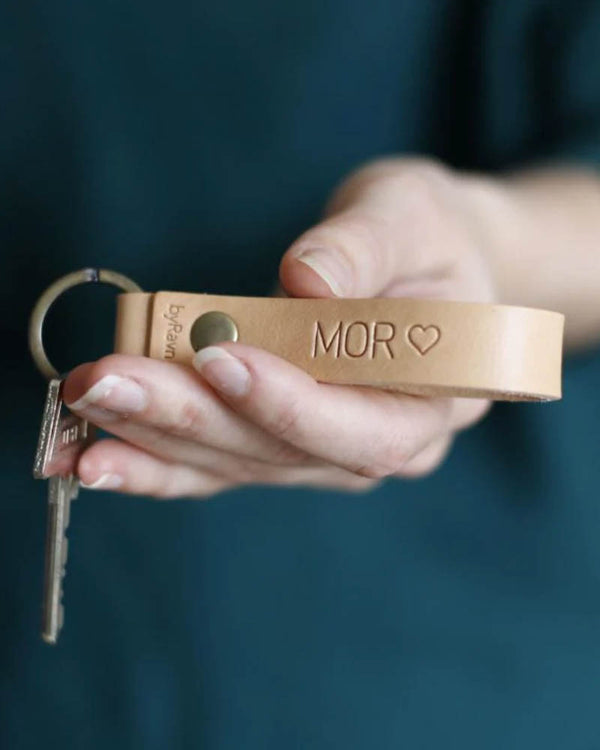 RAVN nøglering i naturfarvet læder med graveringen "Mor" ♡, holdt i hånden med nøgler