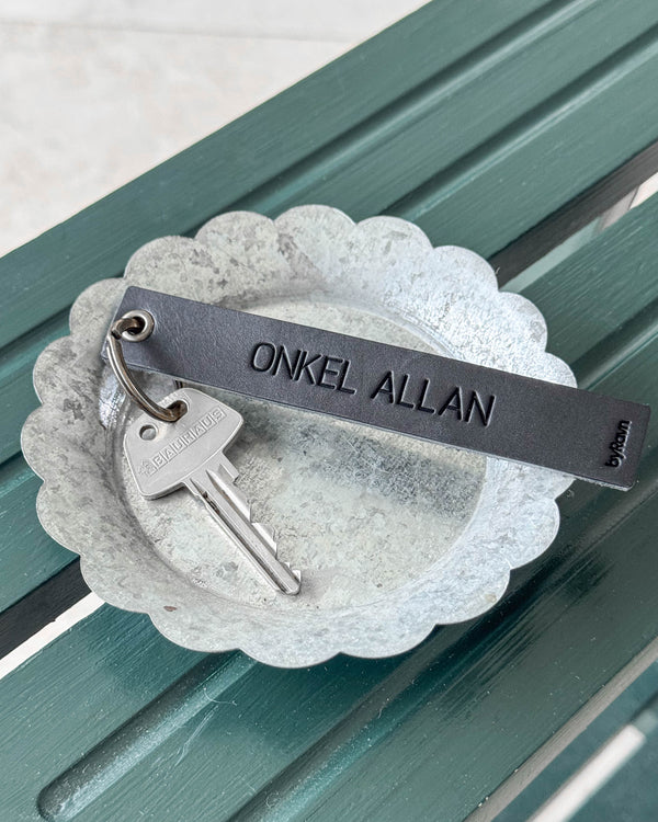 SOLO Large nøglering i sort læder med graveringen "Onkel Allan" og nøgle i zinkskål på grøn bænk