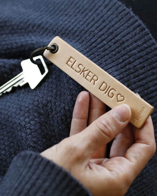 SOLO Medium nøglering i naturfarvet læder holdt i hånden med nøgle og graveringen "Elsker dig" ♡