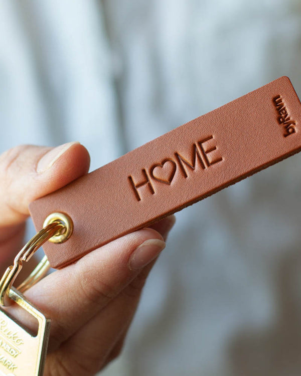 SOLO Small nøglering i cognac læder holdt i hånden med nøgle og graveringen "Home", hvor O'et er et hjerte
