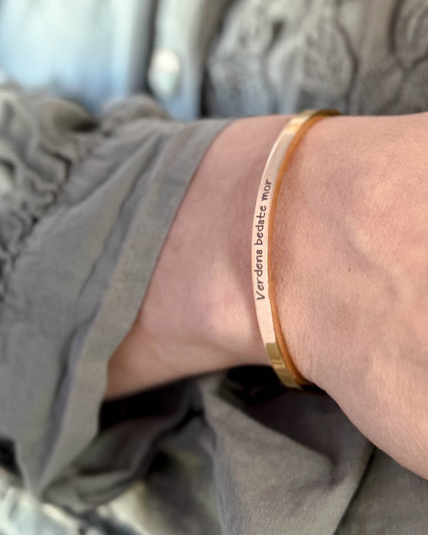 VENUS SCRIPT armbånd i guldbelagt stål med "Verdens bedste mor" i håndskrift om håndleddet, grå bluse