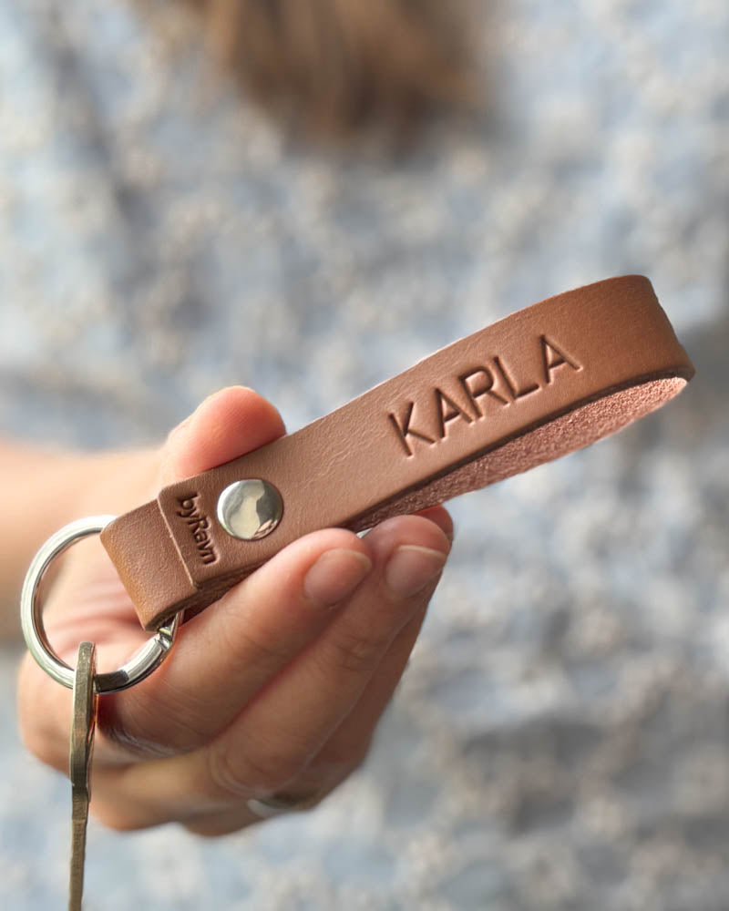 Personlig konfirmationsgave – RAVN nøglering i cognac læder præget med navnet "Karla", holdt i hånden med nøgle