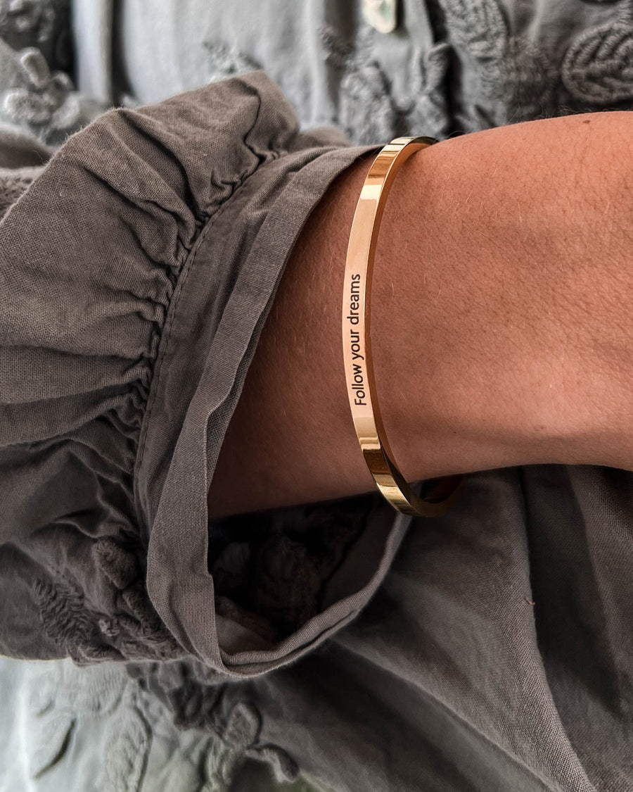VENUS armbånd i guldbelagt stål med graveringen "Follow your dreams" båret om håndleddet