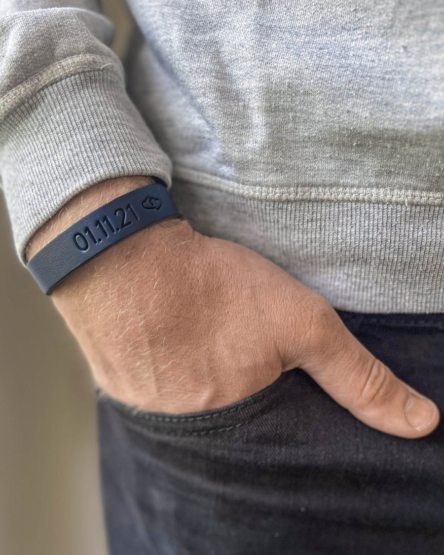 MONO læderarmbånd i mørkeblåt læder med datoen "01.11.21" og lille symbol graveret om håndleddet, hånd i lomme