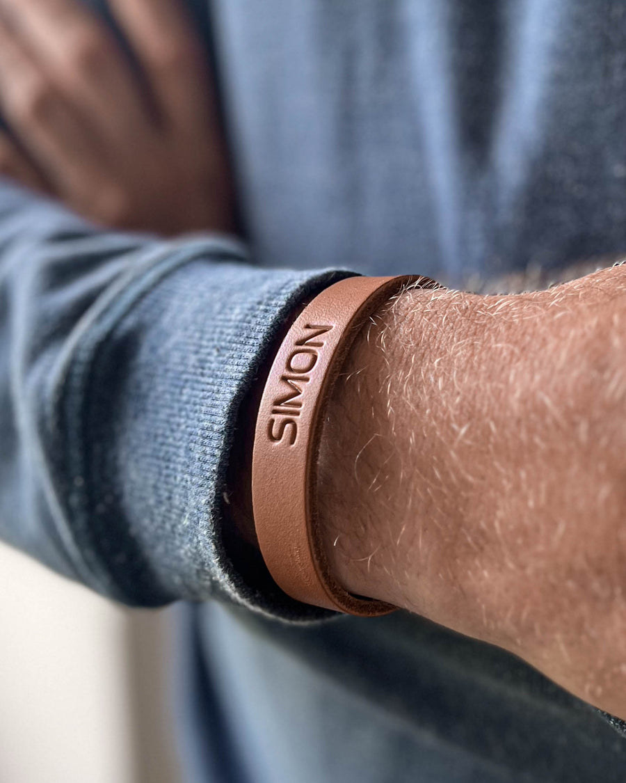 MONO læderarmbånd i cognac læder med navnet "Simon" graveret, båret om håndleddet på mand i blå strik