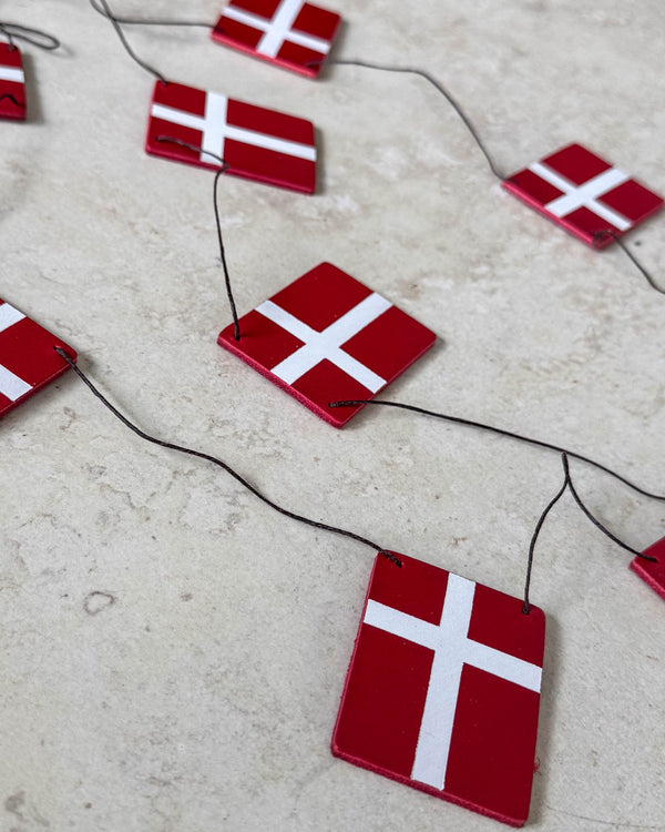 SALUT flagranke med Dannebrog-flag i rødt læder på sort snor lagt på lys stenoverflade