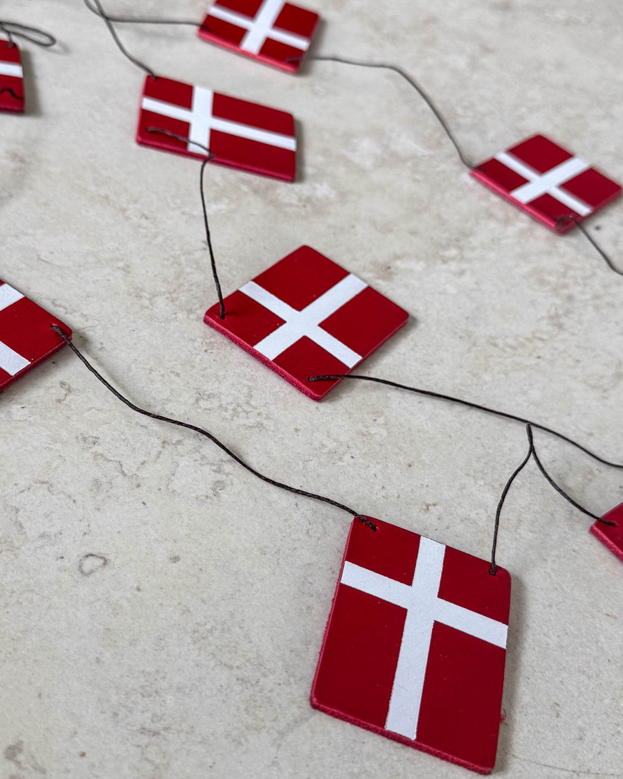 SALUT flagranke med Dannebrog-flag i rødt læder på sort snor lagt på lys stenoverflade