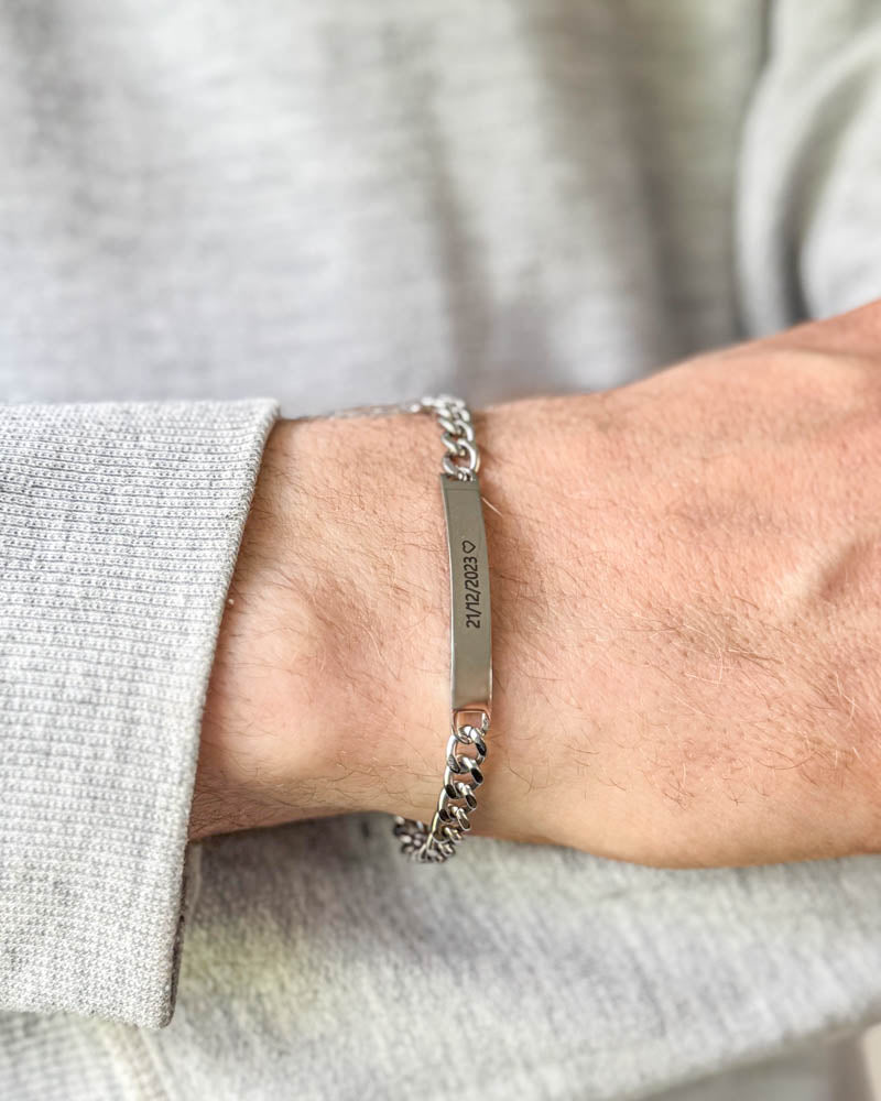 ARA armbånd i sølvfarvet rustfrit stål med datoen "21/12/2023" ♡ graveret, båret om håndleddet til lysegrå sweatshirt