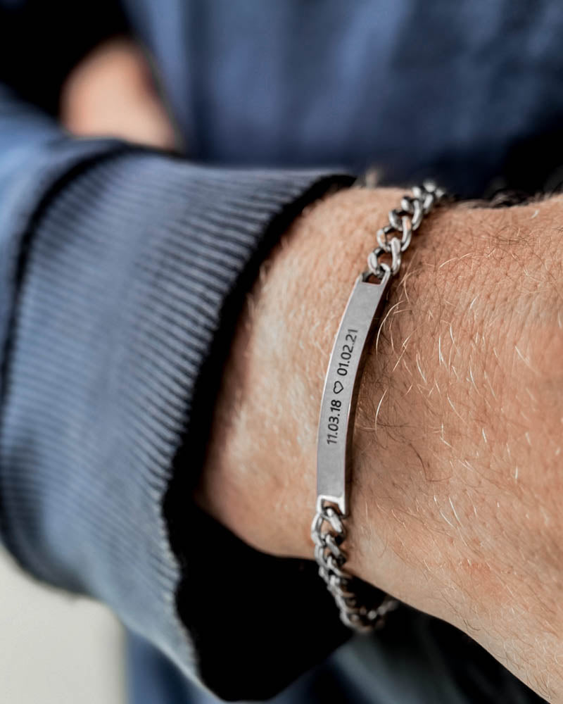 ARA armbånd i sølvfarvet rustfrit stål med datoerne "11.03.18 ♡ 01.02.21" graveret om mandehåndled, blå sweatshirt
