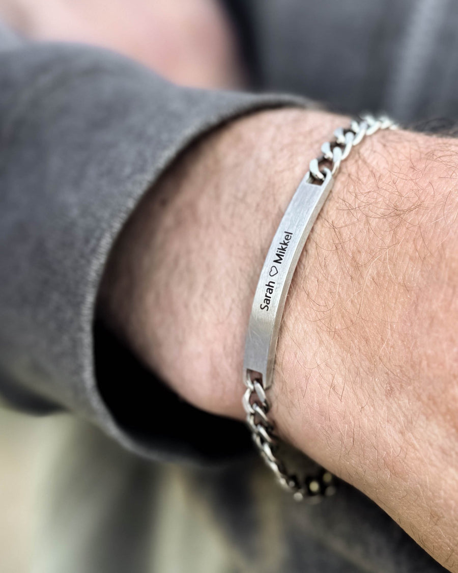 ARA armbånd i børstet sølvfarvet rustfrit stål med graveringen "Sarah ♡ Mikkel" båret om mandens håndled