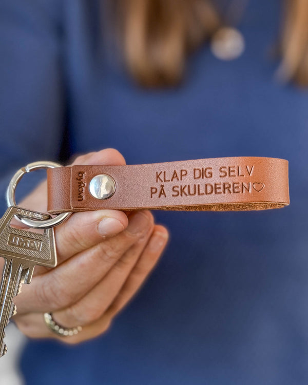 BOND nøglering i cognac læder med graveringen "Klap dig selv på skulderen" ♡, holdt i hånden med nøgler