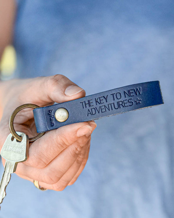 BOND nøglering i mørkeblåt læder med personlig gravering "The key to new adventures" ☆, holdt i hånden med nøgle