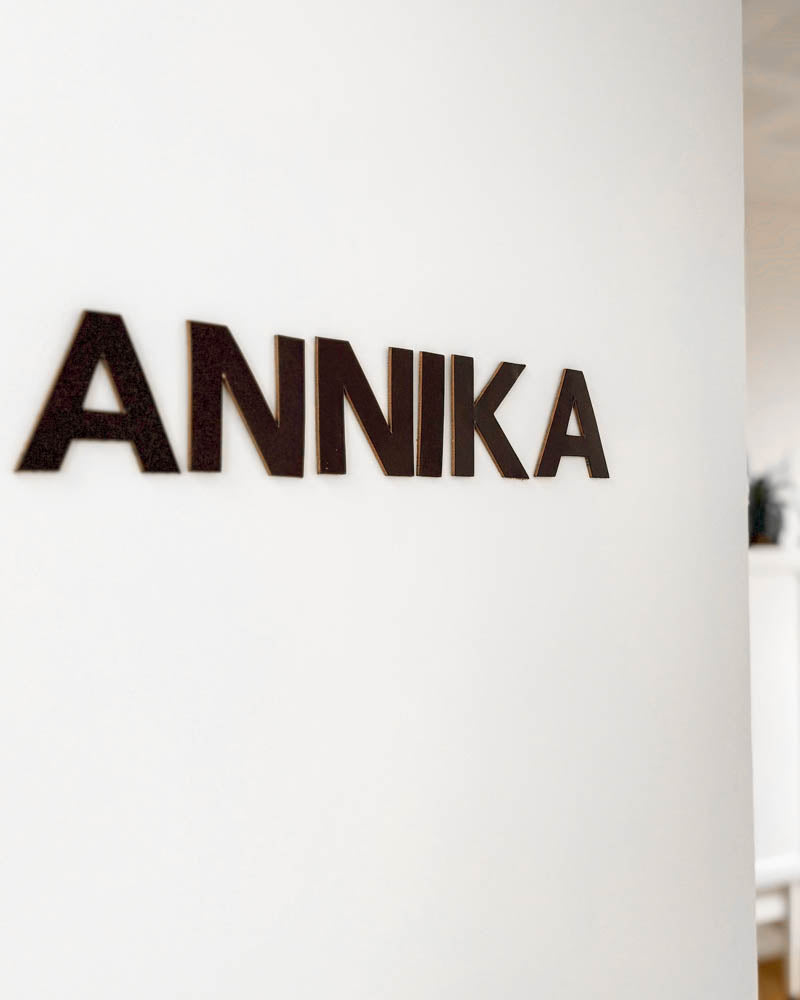 BOX bogstaver i mørkebrunt læder med navnet "Annika" monteret på hvid væg