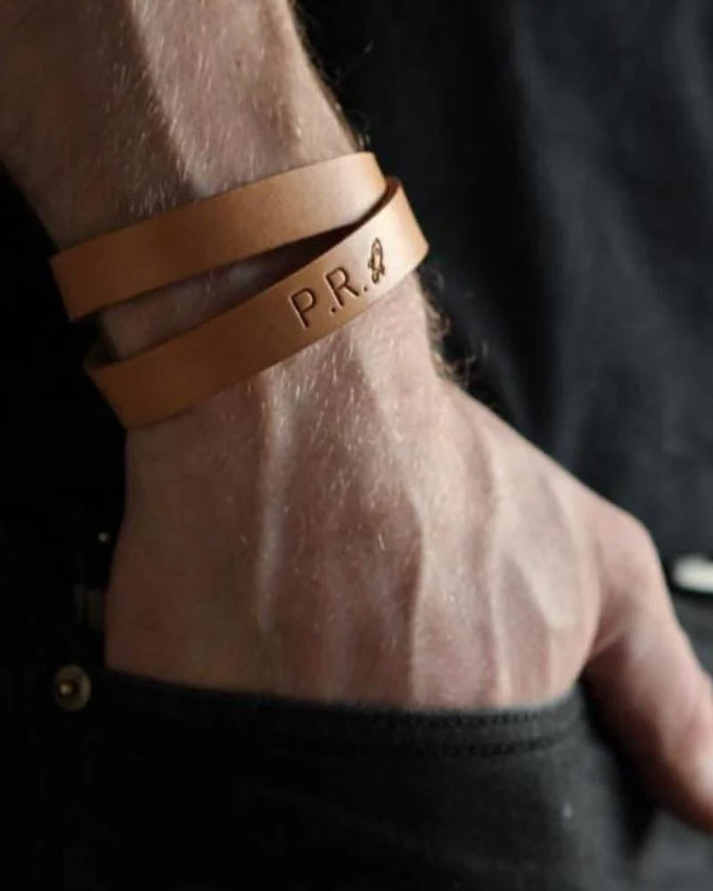 DUO læderarmbånd, her vist i lyst cognacfarvet læder, med initialerne "P.R." og lille motiv graveret om mandehåndled
