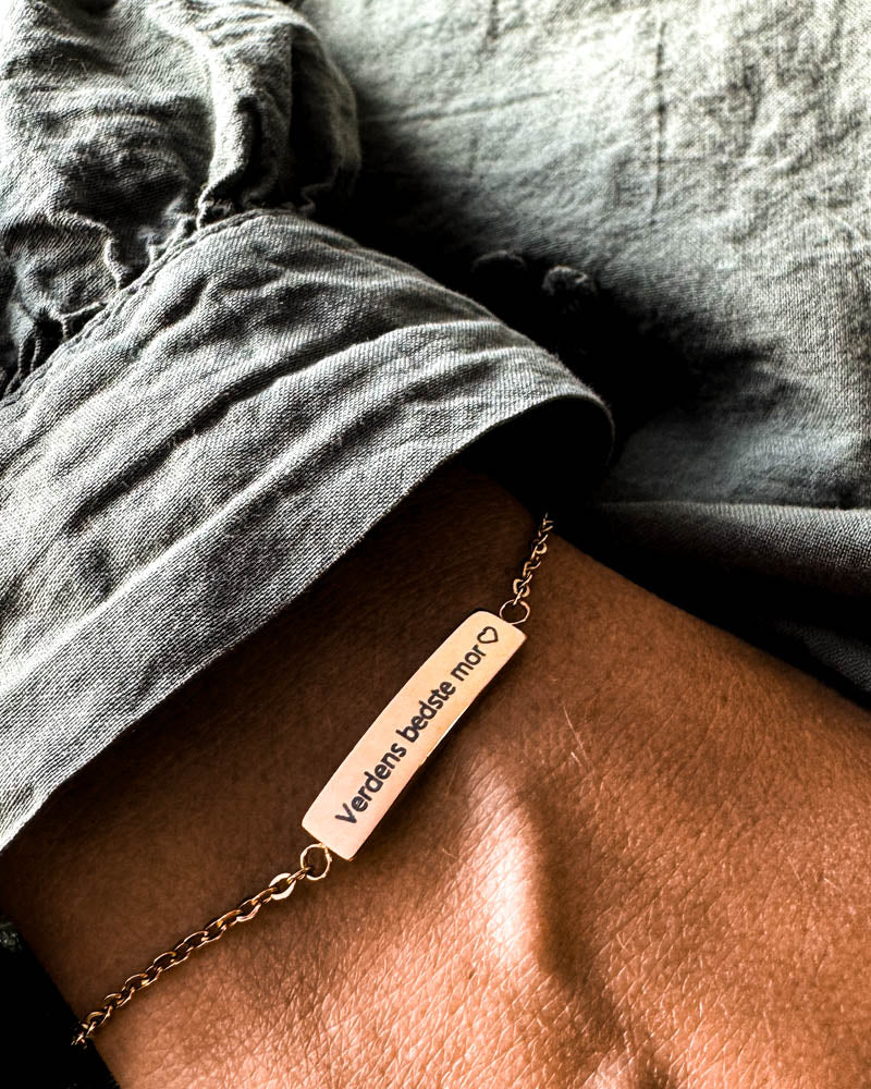 EVI armbånd i guldbelagt stål med graveringen "Verdens bedste mor" ♡ om håndleddet, grå hørskjorte