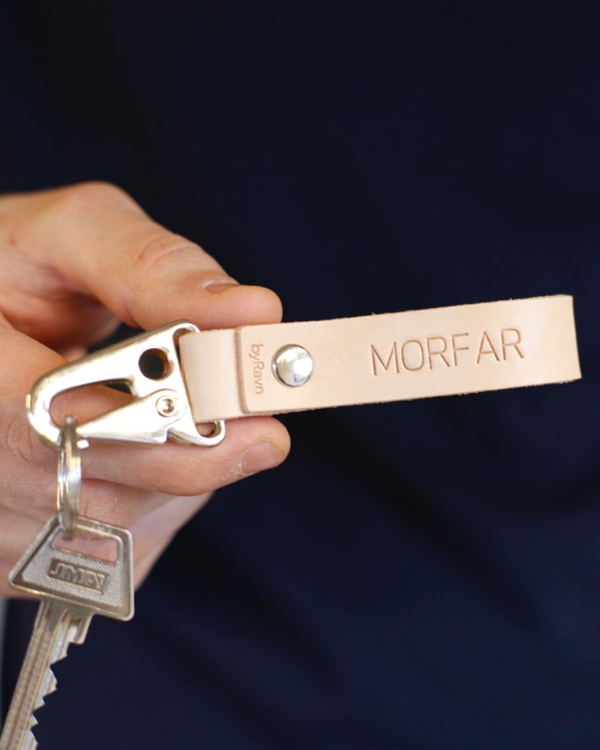 HOOK nøglering i naturfarvet læder med karabinhage i stål og graveringen "Morfar", holdt i hånden med nøgle