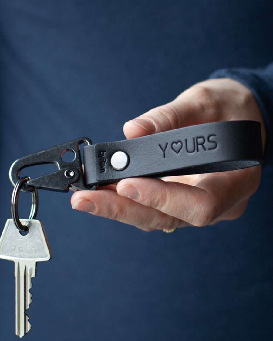 HOOK nøglering i sort læder med graveringen "Y♡urs" og karabinhage i sort stål, holdt i hånden med nøgle