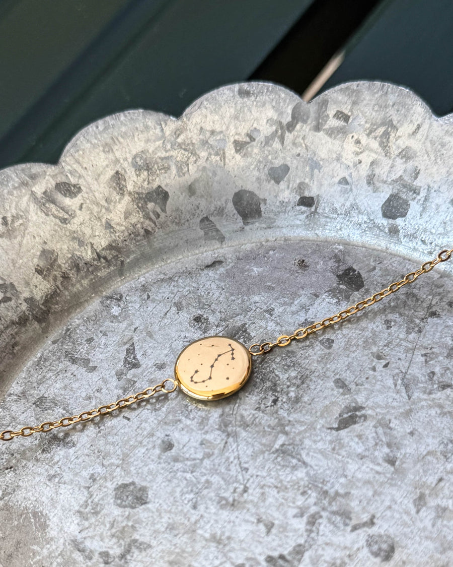IBI STAR armbånd i guldbelagt stål med stjernebilledet Skorpionen graveret på rund plade, liggende på zinkfad