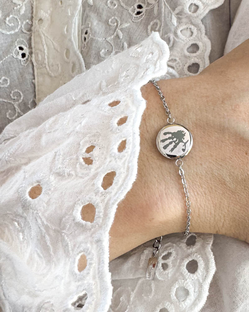 IBI MOTIF armbånd i sølvfarvet rustfrit stål med graveret håndaftryk, båret om håndleddet til hvid blondebluse