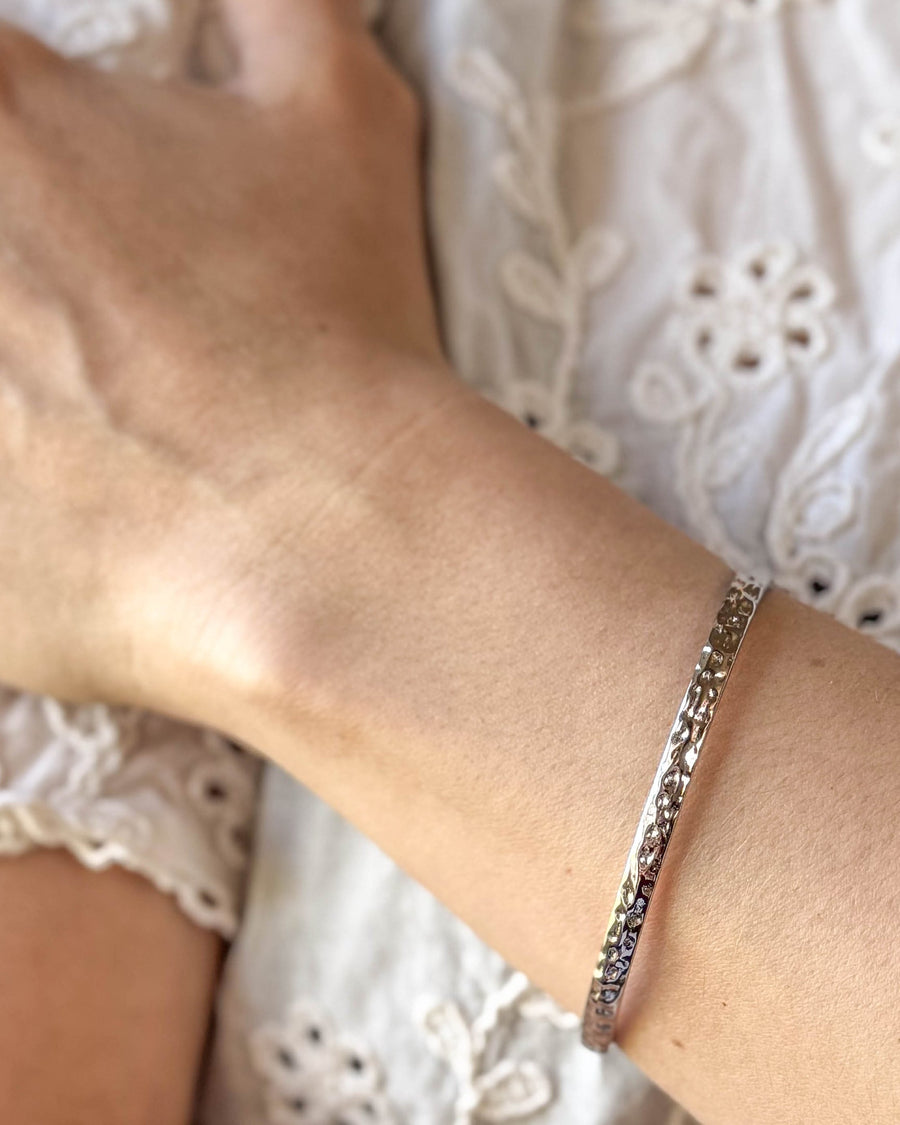 LUNA armbånd i sølvfarvet rustfrit stål, hamret armring båret om håndleddet til hvid blondebluse
