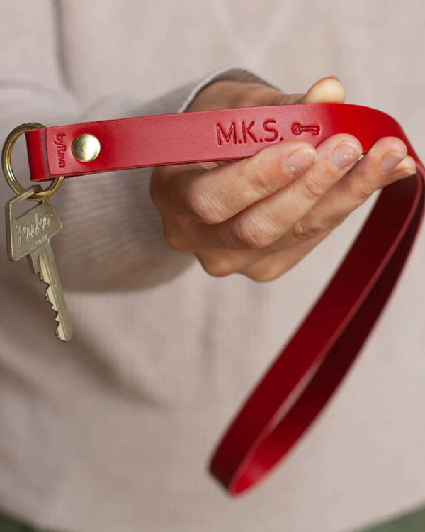 MAX nøglering i rødt læder som lang strop med initialerne "M.K.S." og nøglesymbol graveret, holdt i hånden med nøgle