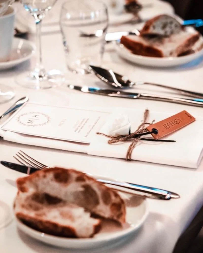 Prøve på MERRY bordkort i cognac læder med navnet "Jeffrey" graveret ved menukort og brød på festbordet