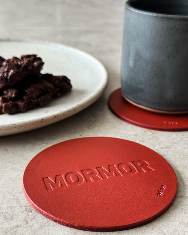 MOKKA bordskåner i rødt læder præget "Mormor" på lyst bord med grå kaffekop og tallerken med chokoladekage
