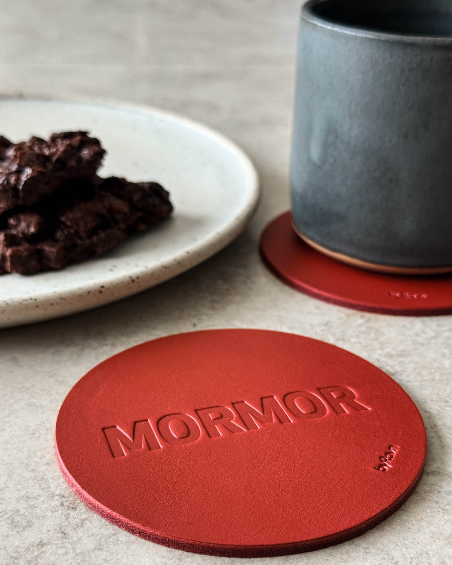 MOKKA bordskåner i rødt læder præget "Mormor" på lyst bord med grå kaffekop og tallerken med chokoladekage