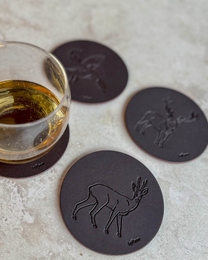 MOKKA jagt bordskånere i mørkebrunt læder præget med råbuk, gråand og kronhjort på lyst bord ved glas whisky