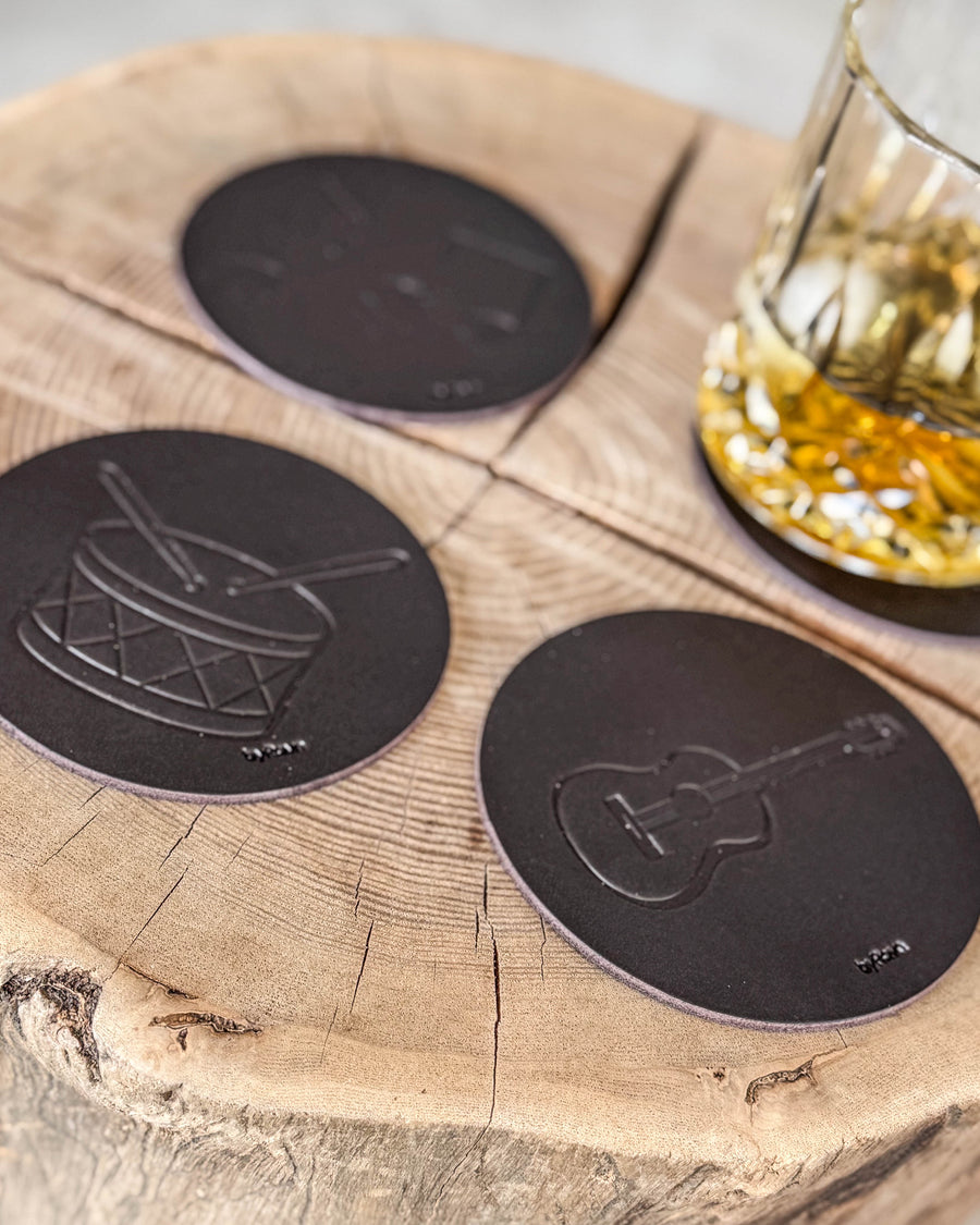 MOKKA musik bordskånere i mørkebrunt læder præget med tromme og guitar på træskive ved krystalglas med whisky