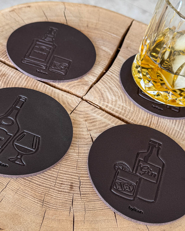 MOKKA spiritus bordskånere i mørkebrunt læder præget med gin, cognac og whisky på træskive ved glas med whisky og is