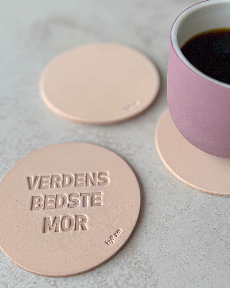 MOKKA bordskånere i naturfarvet læder præget "Verdens bedste mor" på lyst bord med rosa kaffekop