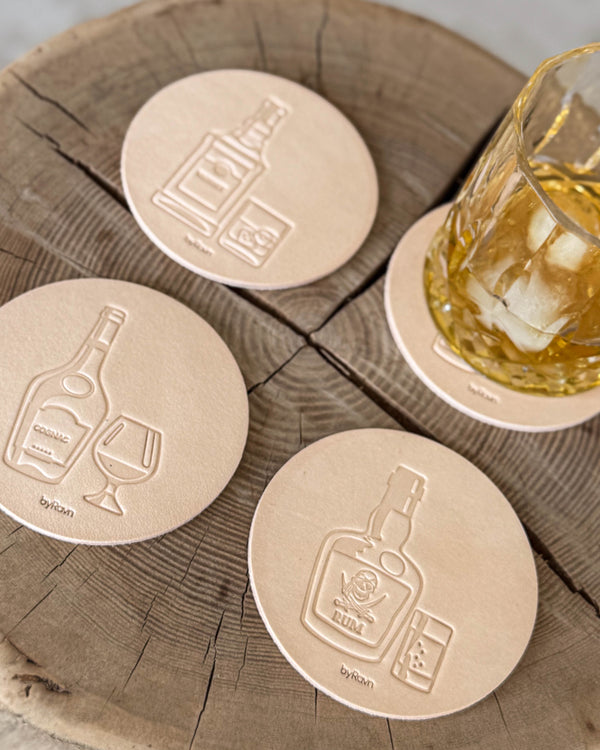 MOKKA spiritus bordskånere i naturfarvet læder præget med cognac, rom og whisky på træskive ved glas med whisky og is