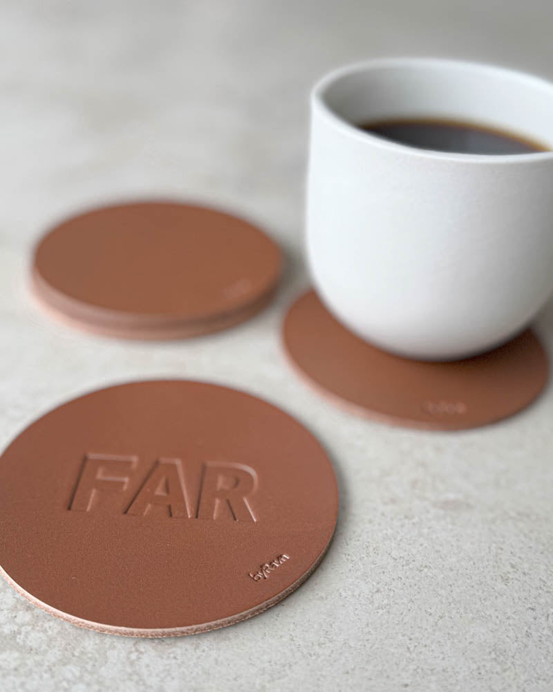 MOKKA bordskåner i cognac læder præget "Far" i store bogstaver, flere coasters og hvid kaffekop bagved