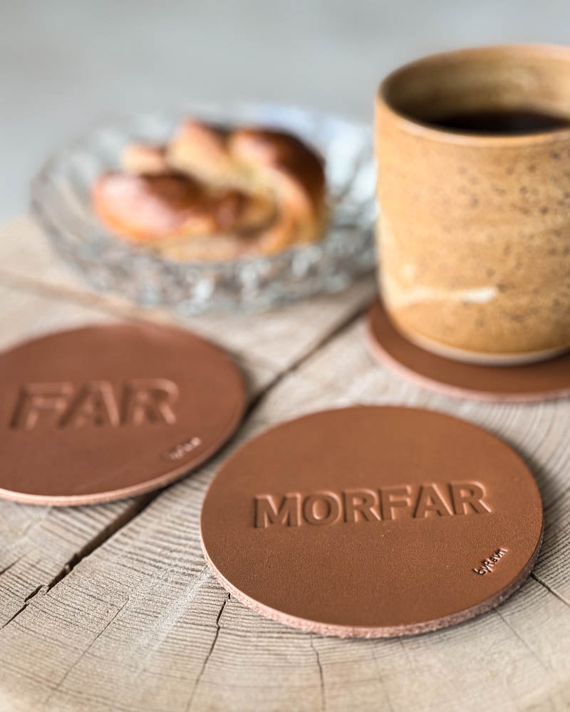 MOKKA bordskånere i cognac læder præget "Far" og "Morfar" på træskive med kaffekop og kanelsnegl på glasfad
