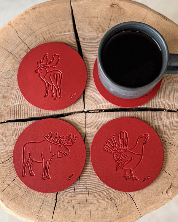 MOKKA jagt bordskånere i rødt læder præget med elg, tjur og dådyr på træskive ved grå kaffekop på coaster