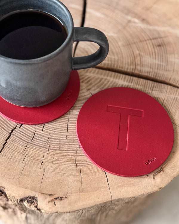 MOKKA bordskåner i rødt læder præget med bogstavet "T" på træskive ved grå kaffekop på coaster