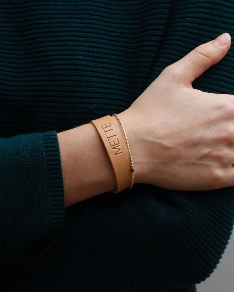 MONO læderarmbånd i naturfarvet læder med navnet "Mette" graveret om håndleddet sammen med tyndt guldarmbånd
