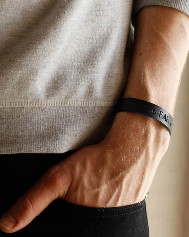 MONO læderarmbånd i sort læder med anker-symbol og graveringen "Far" om håndleddet, hånd i bukselomme