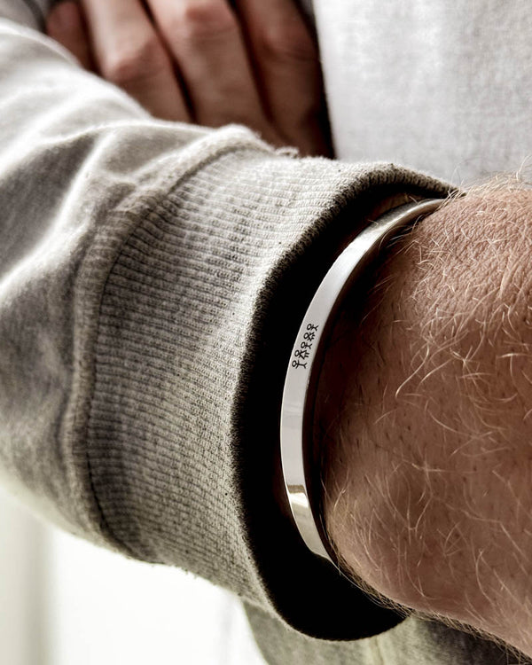MARS STICK armbånd i sølvfarvet rustfrit stål med tændstikfamilie graveret om mandehåndled, lysegrå sweatshirt
